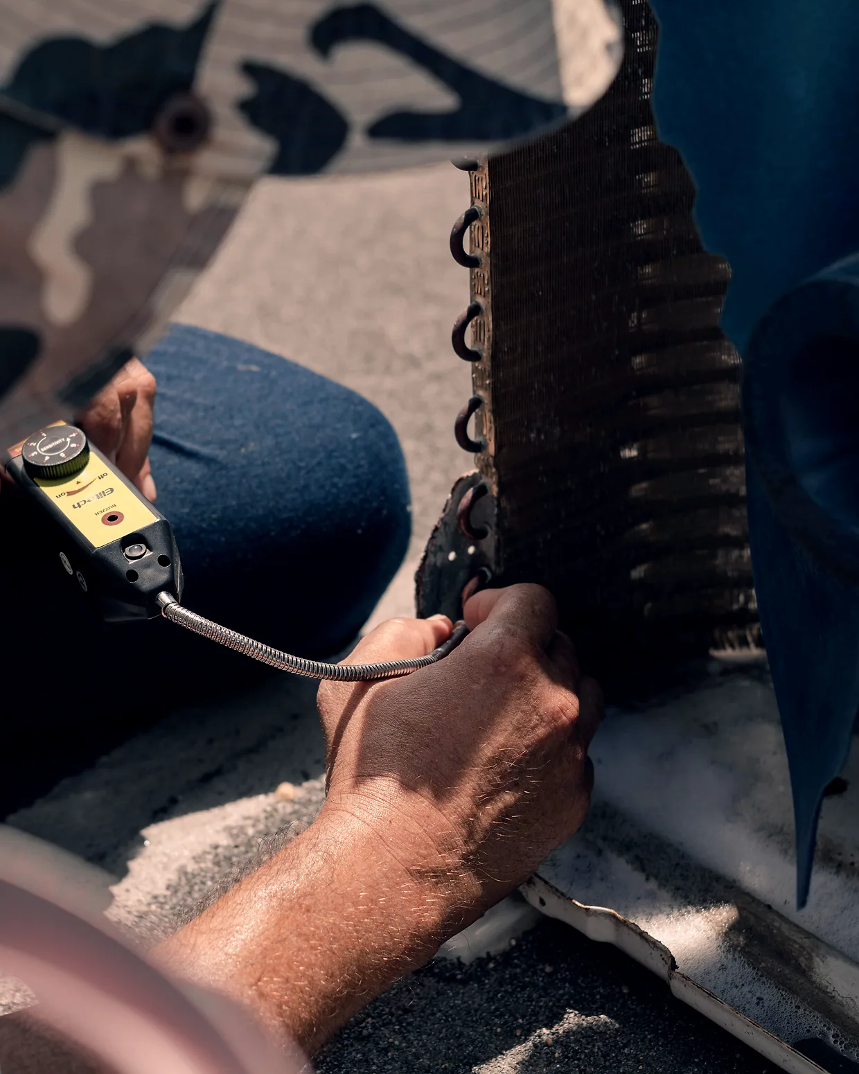 A technician's hands taking a reading at a condenser coil with a meter.