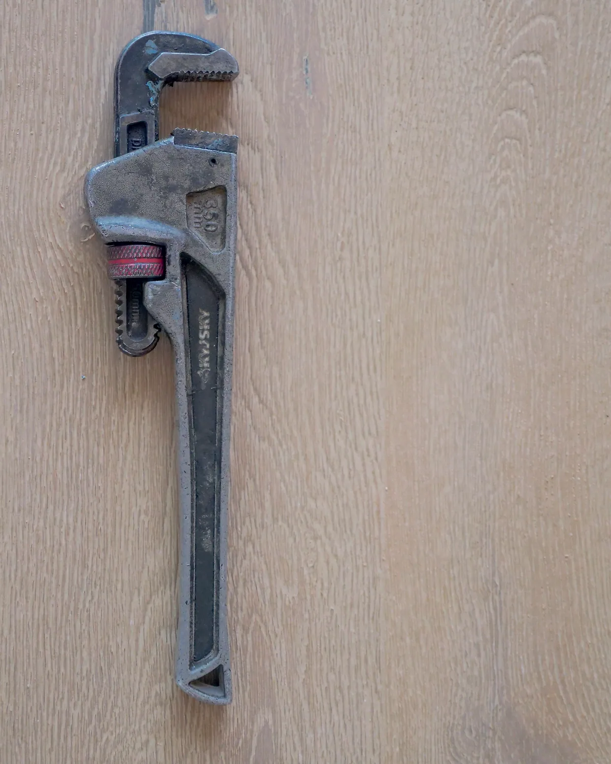 A pipe wrench lying on a pale timber bench.